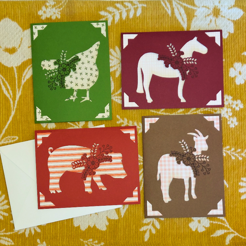 Four greeting cards with animal illustrations on a floral fabric background