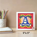 Colorful framed artwork with 'ACOSTA' on a desk with stationery items.