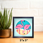 Framed artwork of two pink flamingos on a blue background with a potted plant beside it.
