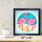 Framed artwork of two pink flamingos on a light blue background, displayed on a wooden surface with a neutral wall.