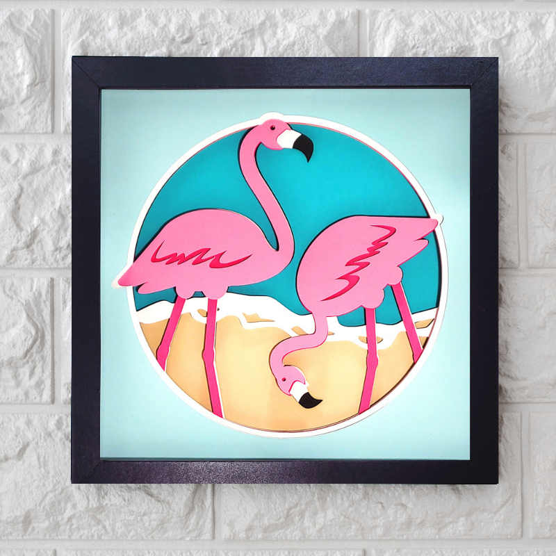 Framed artwork of two pink flamingos on a beach with a blue sky.