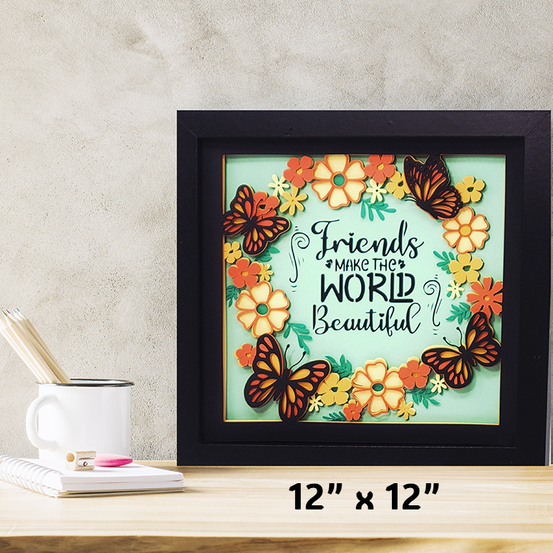 Framed artwork with butterflies and flowers on a table with a mug and notebook.