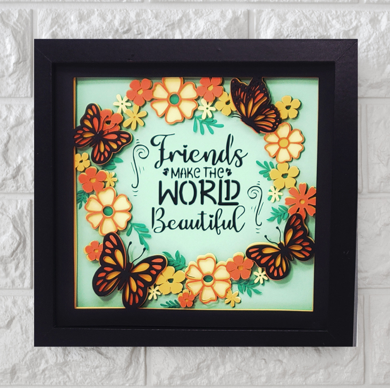 Framed artwork with butterflies and flowers and the quote 'Friends make the world beautiful' on a light blue background.