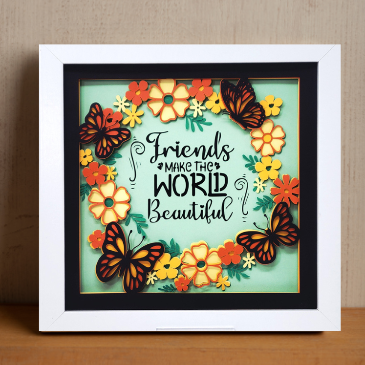 Framed artwork with butterflies and flowers and the quote 'Friends make the world beautiful' on a wooden surface.