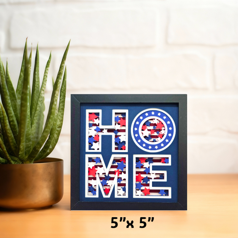 Framed decorative art with 'HOME' design on a table next to a plant