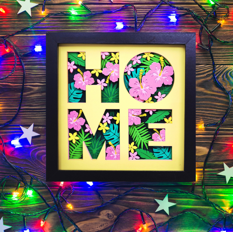 Decorative wall art with 'HOME' letters surrounded by floral patterns on a wooden background with string lights.