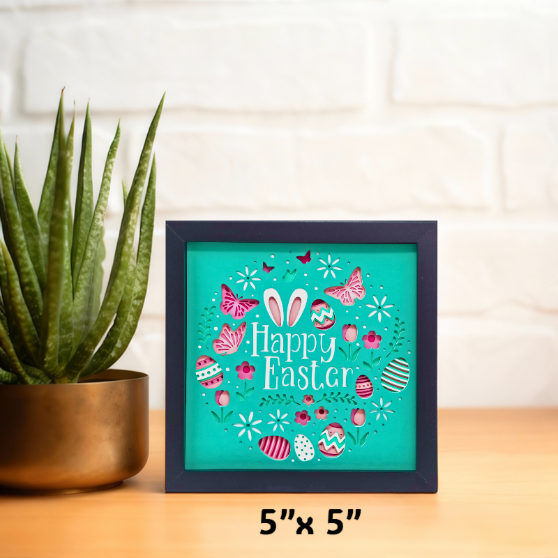 Framed 'Happy Easter' sign with decorative elements on a table next to a plant.