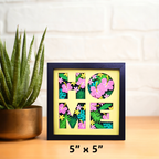 Decorative wall art with 'HOME' letters made of flowers on a wooden surface with a plant.