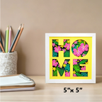 Framed decorative sign with 'HOME' letters on a desk with stationery items.