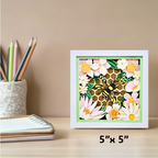 Decorative wall art with flowers and a bee on a 5x5 inch frame, placed on a desk with stationery items.