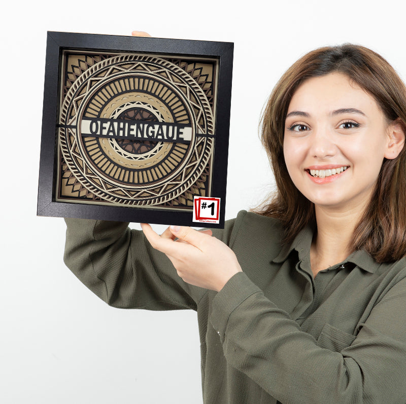 Woman holding a framed decorative wall art with 'Ofahengaue' text on a white background