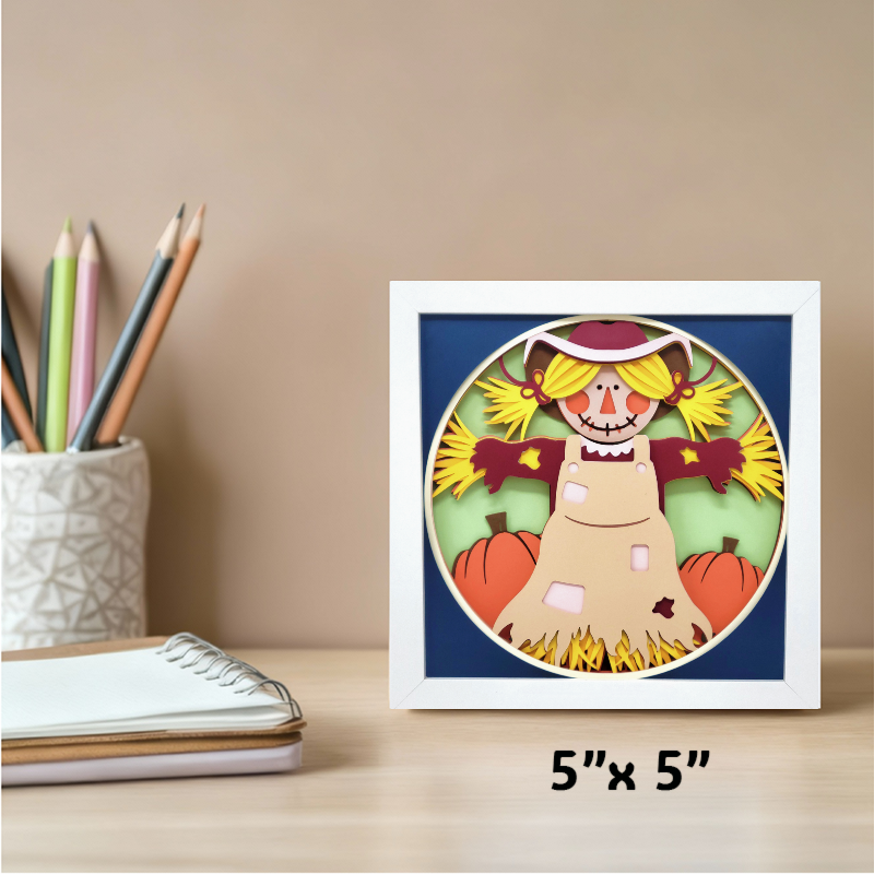 Framed artwork of a scarecrow with pumpkins on a desk with stationery items.