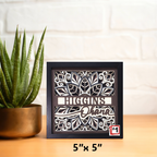 Decorative shadow box with cut-out design and text, placed on a surface with a plant in the background.