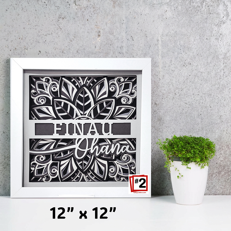 Framed decorative wall art with floral design and text on a gray surface with a plant.