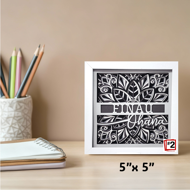 Decorative framed artwork with cut-out design and text on a desk with stationery items.