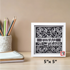 Decorative framed artwork with cut-out design and text on a desk with stationery items.