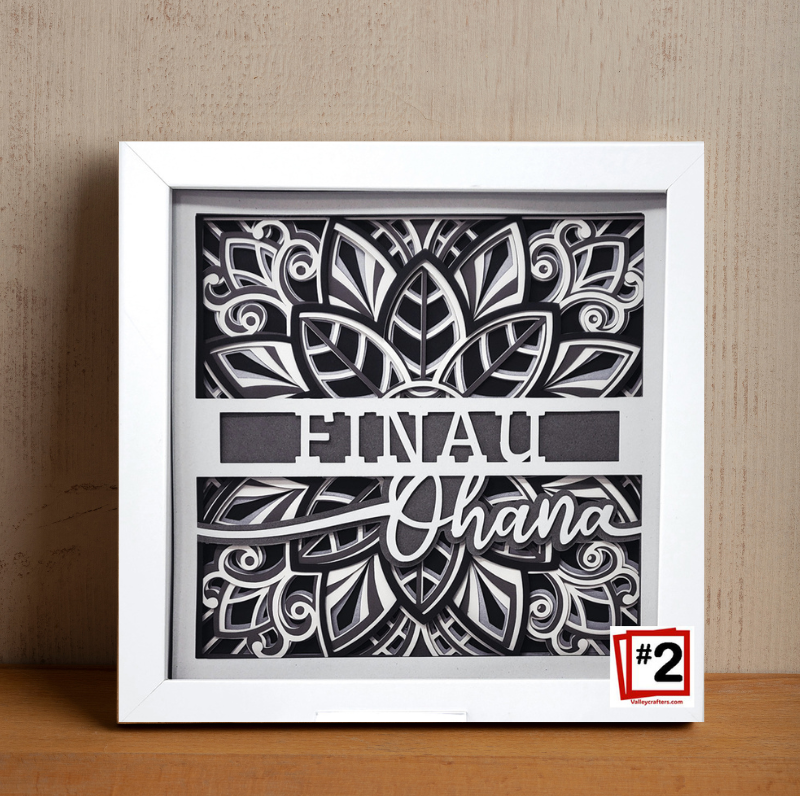 Decorative wall art with black cut-out design and 'Einau Ohana' text in a white frame.