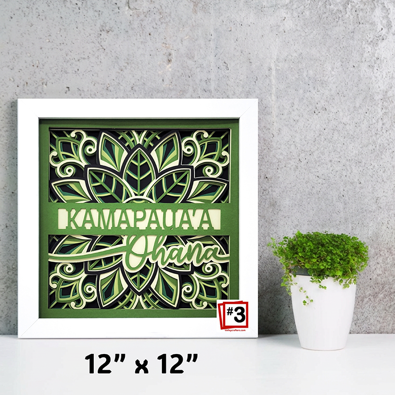 Decorative wall art with green and white design on a gray wall with a plant.