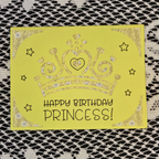 Yellow card with a crown illustration and 'Happy Birthday Princess!' text on a textured surface.