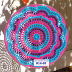 Colorful crocheted sun catcher with spiral pattern on a plain background