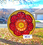 Decorative sun catcher with red and gold colors hanging outdoors.