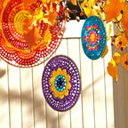Colorful circular decorations hanging on a white wooden fence with autumn leaves.