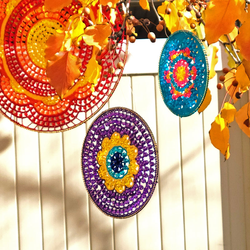 Colorful circular decorations hanging on a white wooden fence with autumn leaves.
