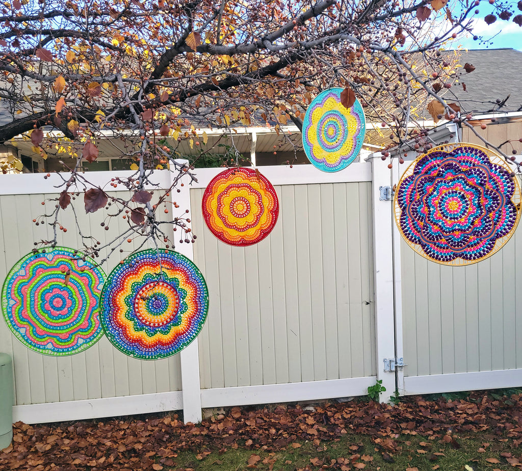 Colorful circular patterns hanging from a tree in front of a white fence.