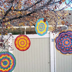 Colorful circular patterns hanging from a tree in front of a white fence.