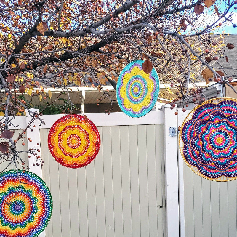 Colorful circular patterns hanging from a tree in front of a white fence.