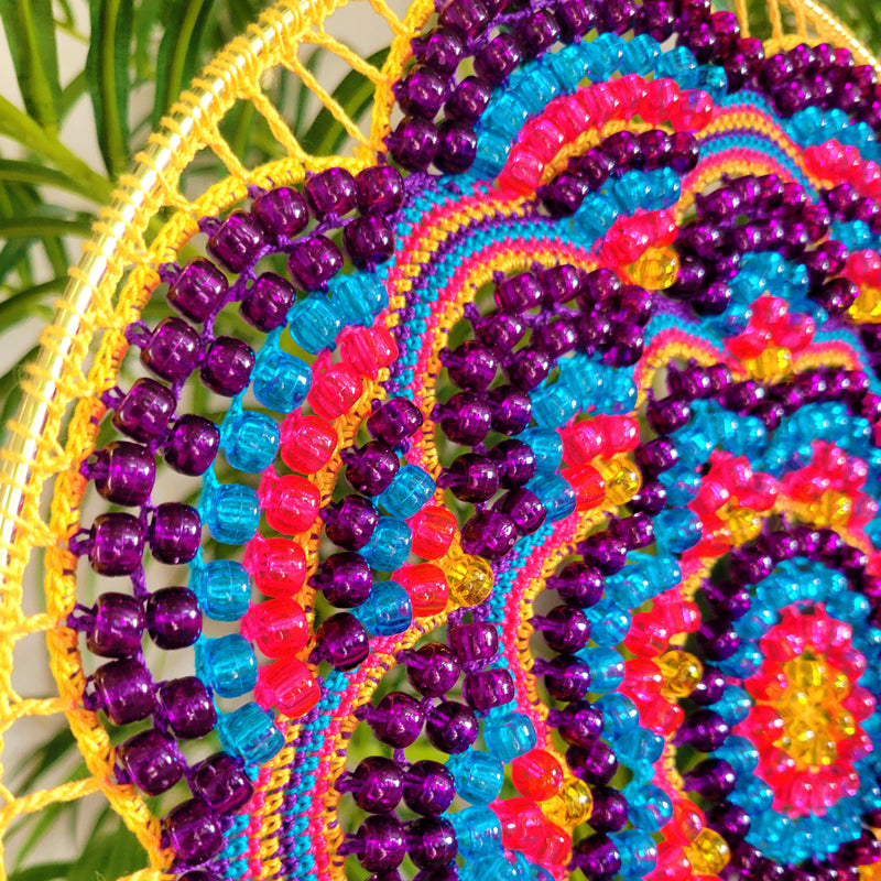 Colorful beaded woven item with a circular pattern against a natural background