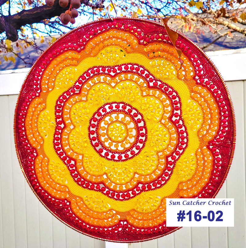 Round crochet suncatcher with red and yellow colors against a white fence background.