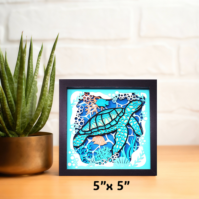 Framed artwork of a turtle with ocean design on a table next to a plant
