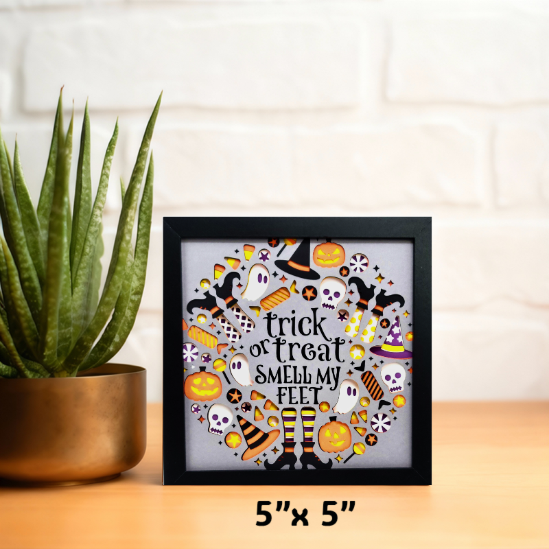 Halloween-themed decorative box with text 'trick or treat smell my feet' on a wooden surface with a plant.