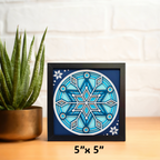 Framed blue geometric art piece on a wooden surface with a plant in the background
