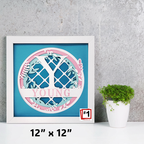 Framed artwork with 'YOUNG' text and decorative elements on a blue background, placed on a gray surface with a plant.