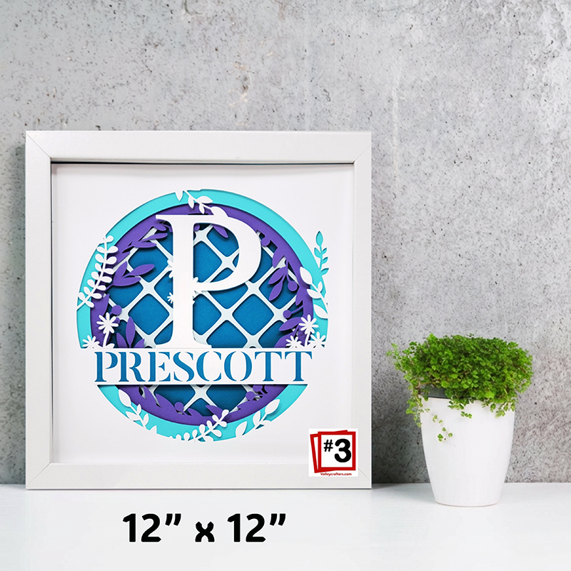Framed decorative artwork with a monogram and name 'Prescott' on a gray wall background.