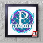 Framed decorative monogram with 'PRESCOTT' on a white background, mounted on a textured wall.