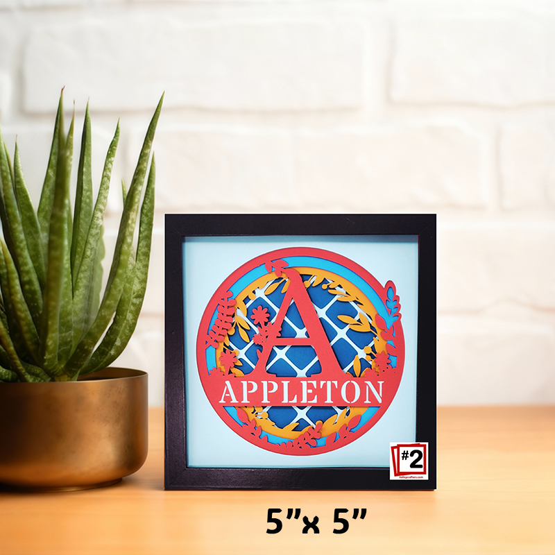 Framed artwork with 'APPLETON' design on a table next to a plant