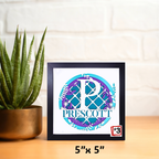 Framed artwork with 'Prescott' design on a wooden surface next to a plant