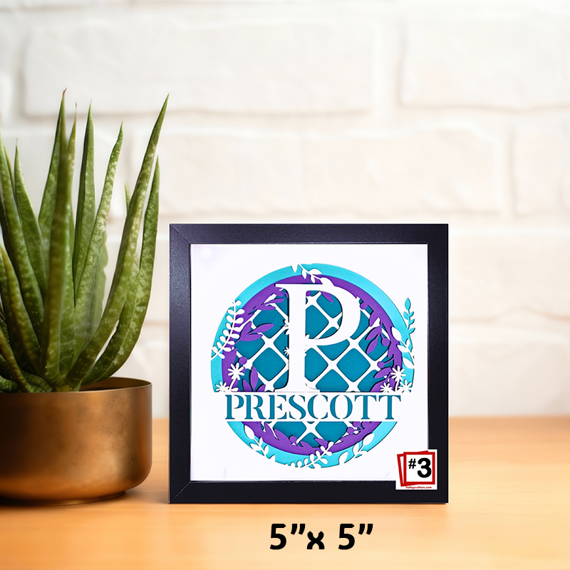 Framed artwork with 'Prescott' design on a wooden surface next to a plant