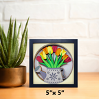 Framed artwork of colorful tulips on a wooden surface with a plant in the background