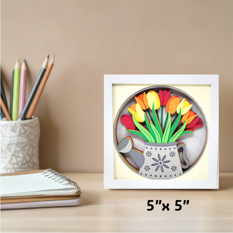 Decorative wall art with tulips and a watering can in a white frame, placed on a desk with stationery items.
