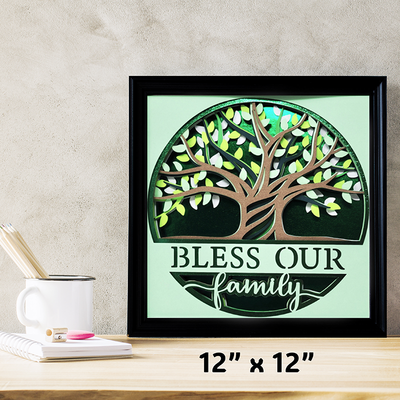 Framed artwork with a tree design and 'Bless Our Family' text on a light green background, placed on a wooden surface.