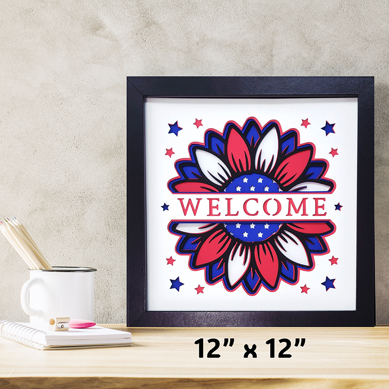 Framed artwork with a floral design and 'WELCOME' text on a white background, placed on a wooden surface.