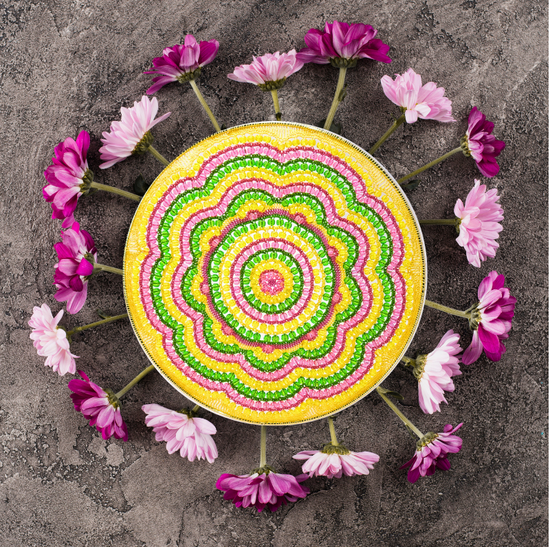 Colorful circular design with pink flowers arranged around it on a gray surface