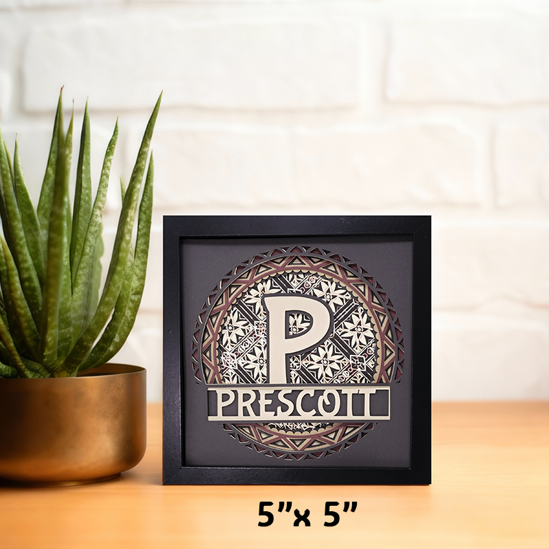 Decorative framed item with 'PRESCOTT' text and plant on a wooden surface