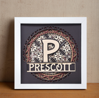 Decorative framed piece with a stylized 'P' and 'Prescott' text on a wooden surface.