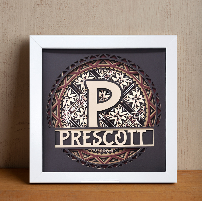 Decorative framed piece with a stylized 'P' and 'Prescott' text on a wooden surface.