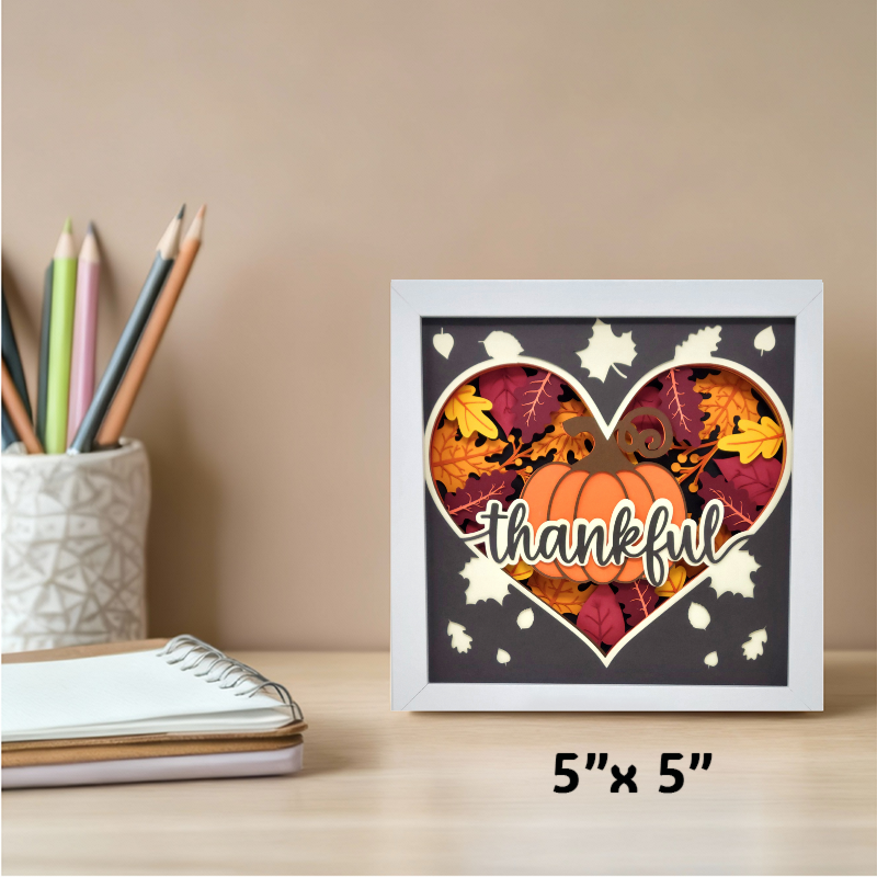 Framed decorative sign with pumpkin and leaves design on a desk with stationery items.